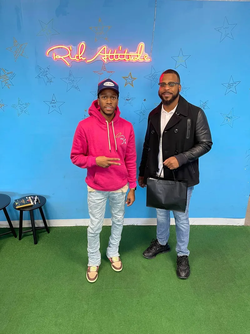 Miguel Jones with a friend in front of a Rich Attitude neon sign