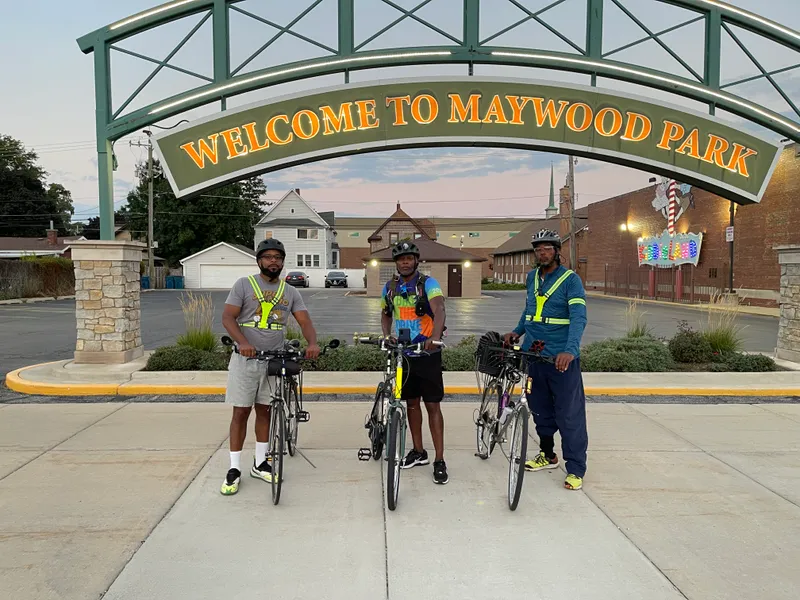 Three cyclists under the Welcome to Maywood Park arch